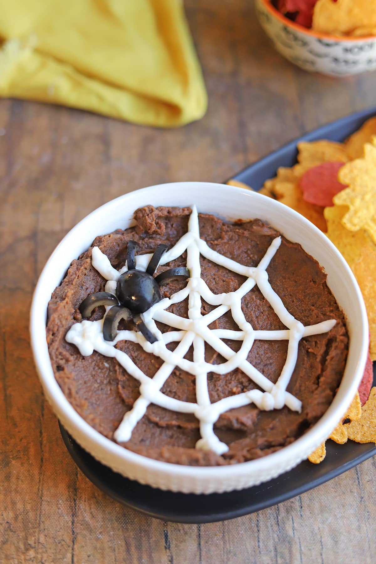 Halloween dip with vegan sour cream spider web and black olive spider in bowl by tortilla chips.