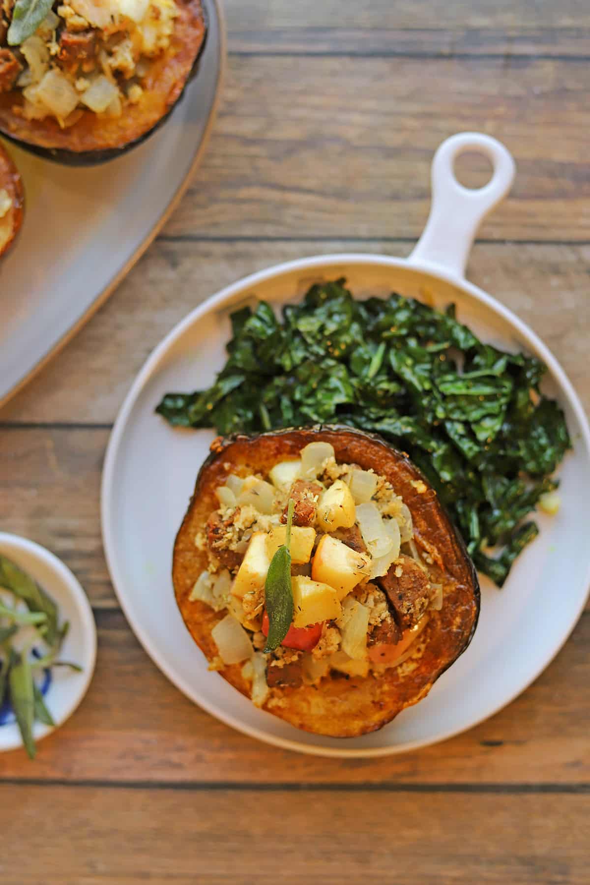 Vegan stuffed acorn squash with apple and seitan sausage on plate with side dish.