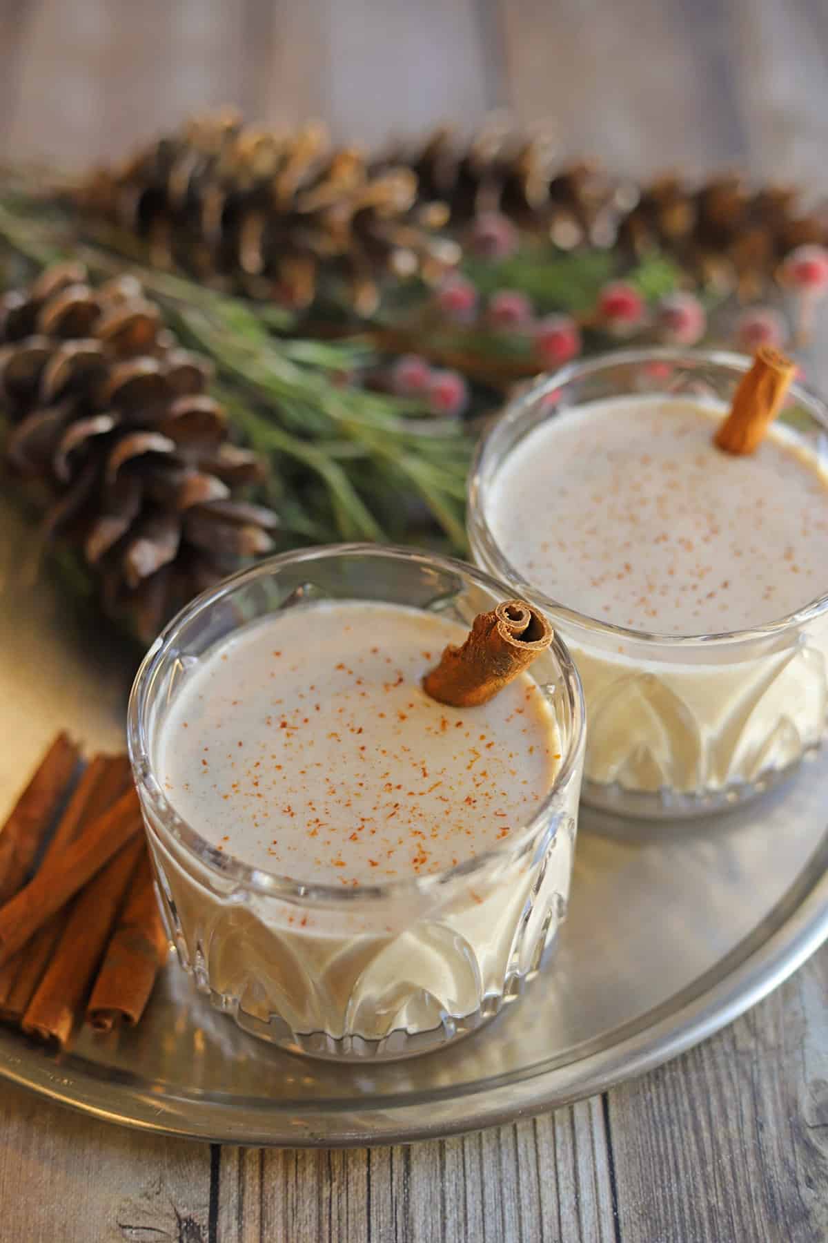 Glasses of egg-free eggnog on table with cinnamon sticks.