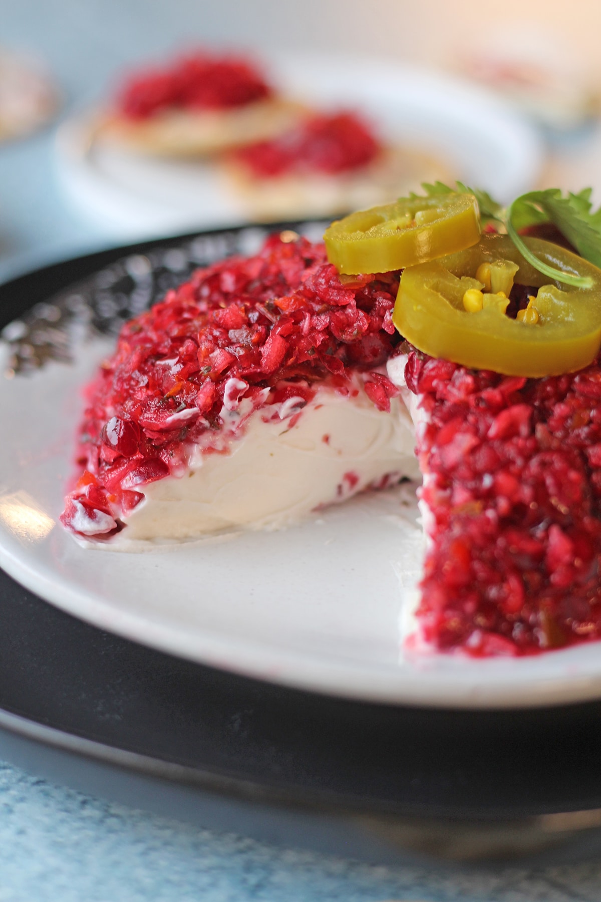 Vegan cranberry cream cheese dip with jalapenos on plate with wedge cut out.