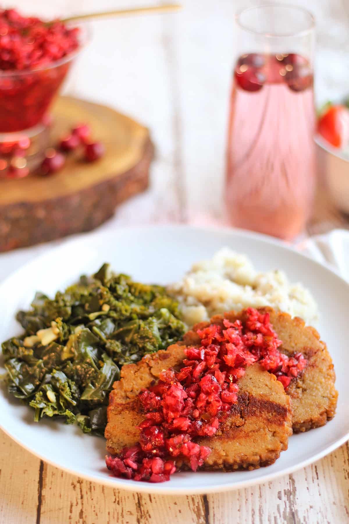 Cranberry salsa over slices of Field Roast Celebration roast on plate with collards and mashed potatoes.