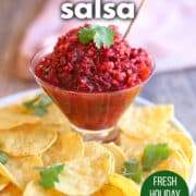 Text overlay: Cranberry salsa, fresh holiday relish, get the recipe at cadryskitchen.com. Bowl of cranberry salsa with jalapeno and cilantro garnish surrounded by tortilla chips.
