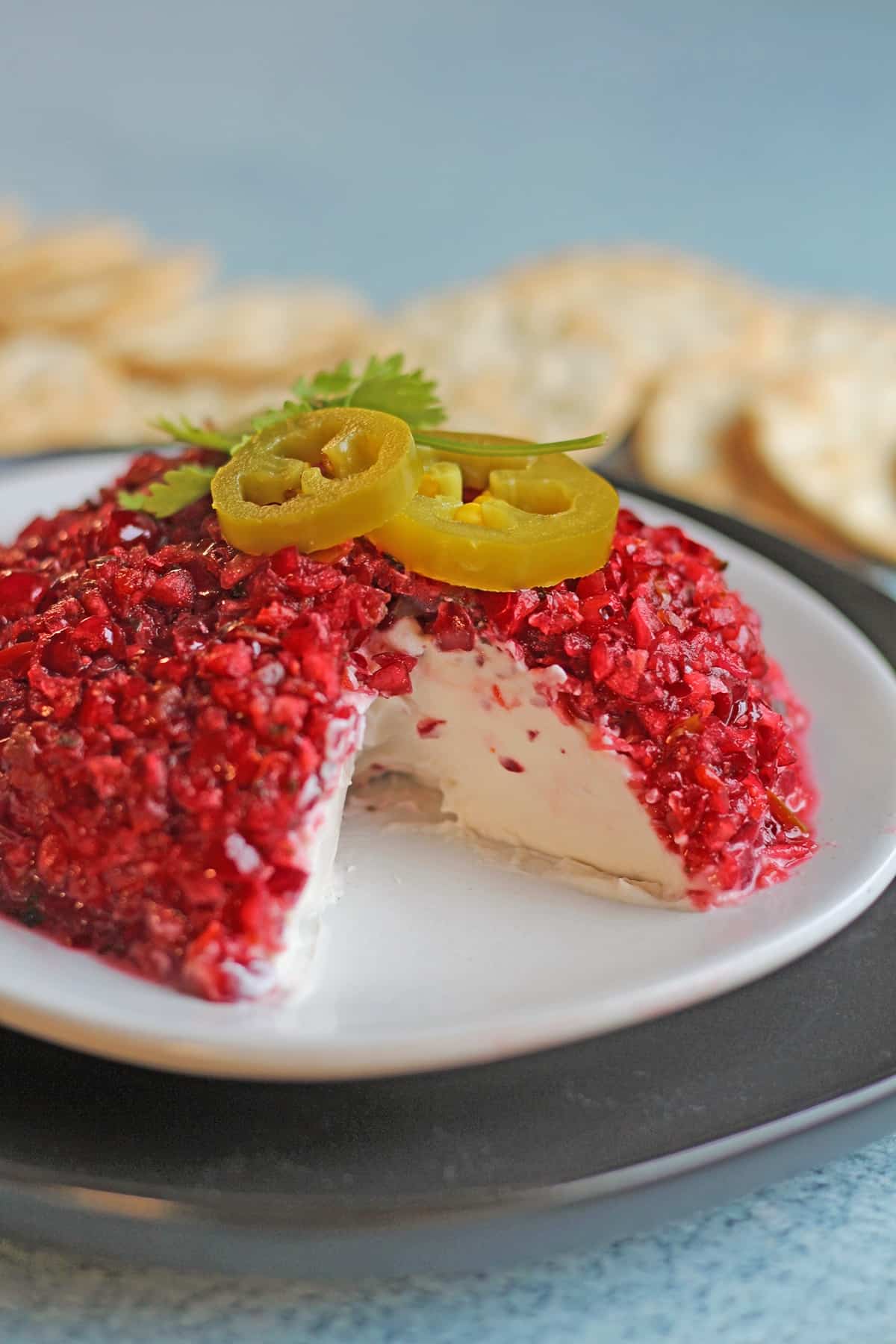 Cranberry jalapeno cream cheese dip on plate with pickled jalapenos and cilantro for garnish.