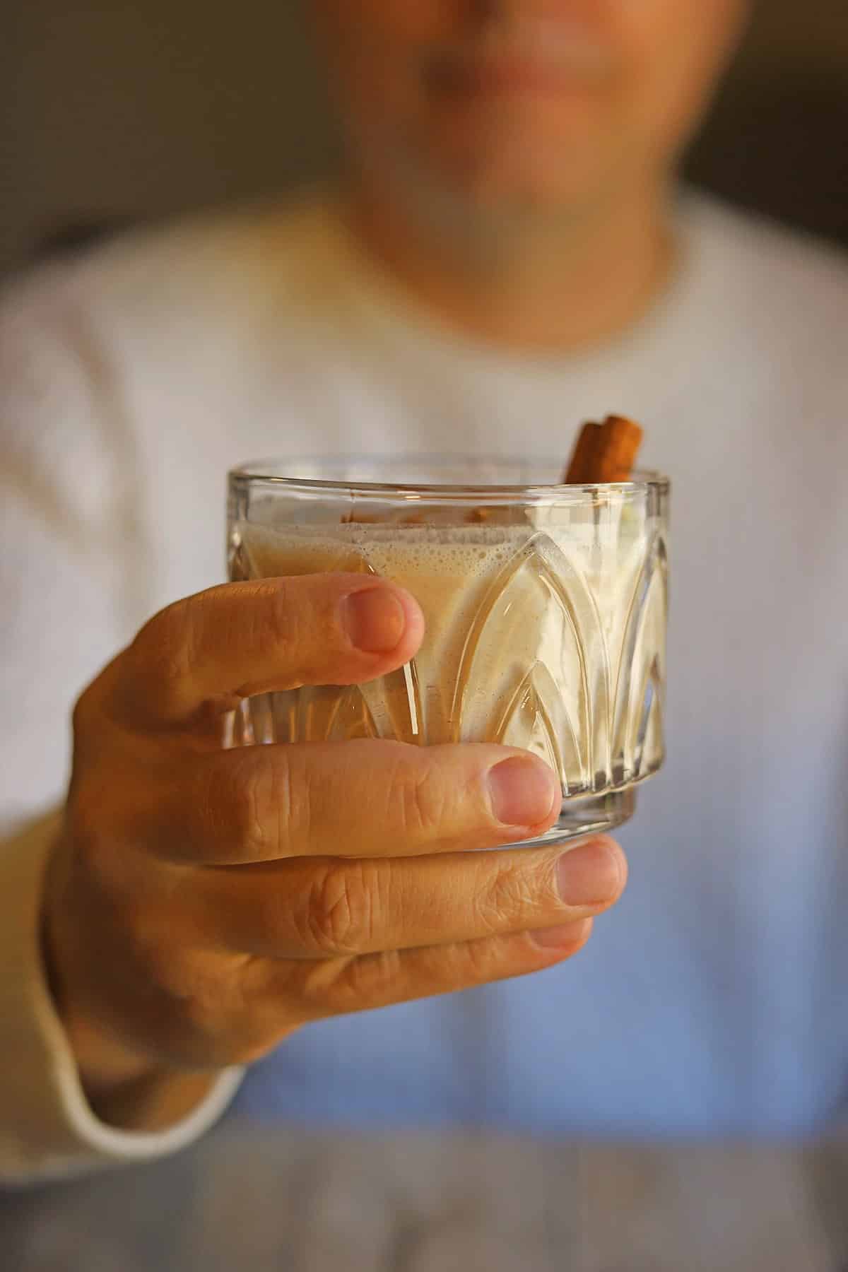 Hand holding glass of vegan eggnog.