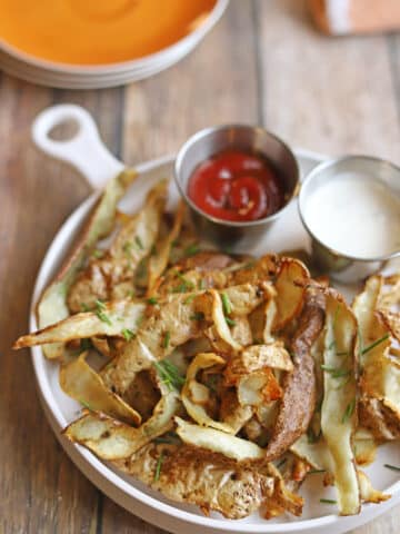 Crisp potato peels with dipping sauces on plate with sauces.