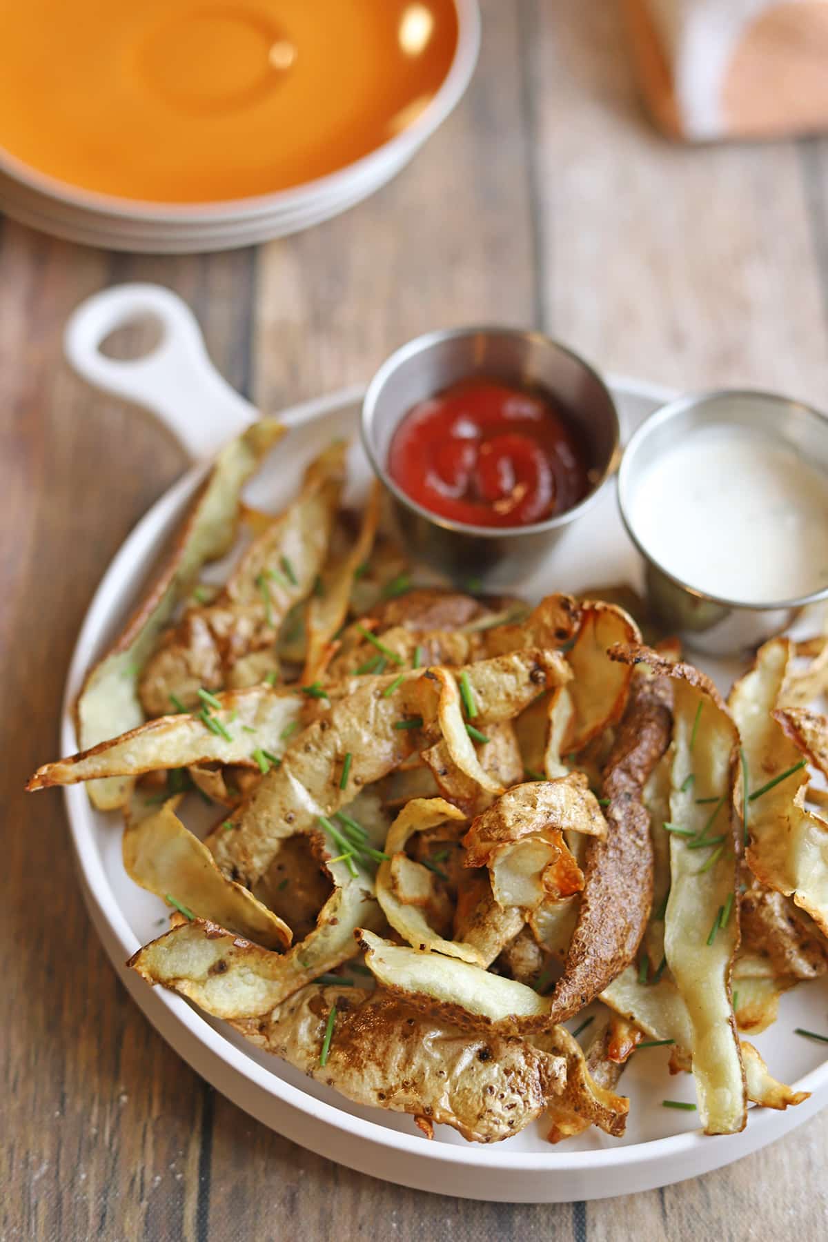 Crisp potato peels with dipping sauces on plate with sauces.
