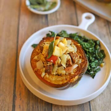 Vegan stuffed squash with sausage and apple Thanksgiving main course on plate with kale side dish.