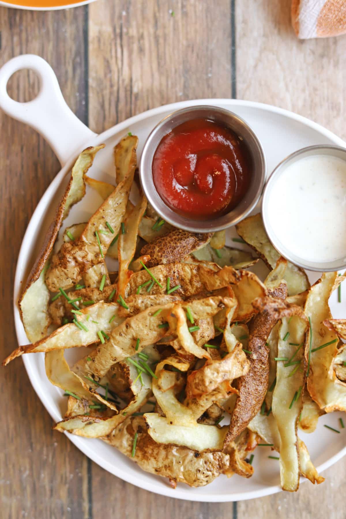 Air fryer potato peels with chives garnish, ketchup, and vegan salad dressing.