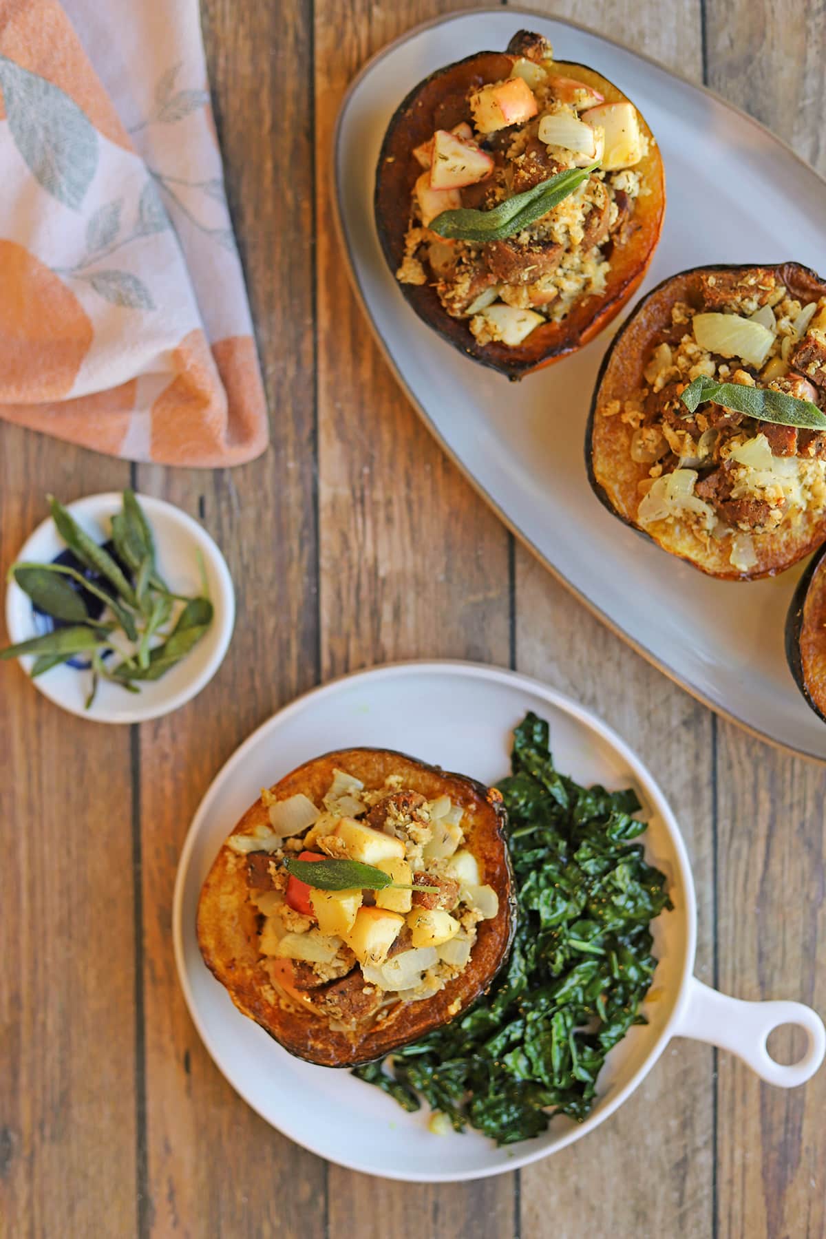 Apple and vegan sausage stuffed acorn squash on platter and plate with fried sage.