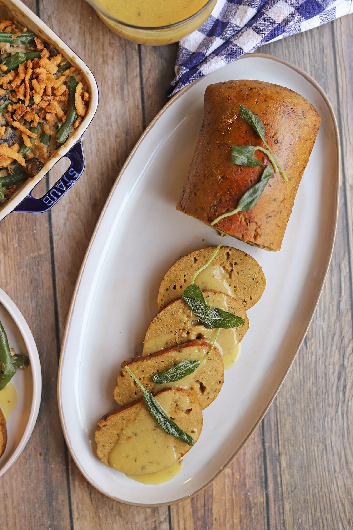 Sliced vegan turkey roast on platter with gravy and fried sage leaves.