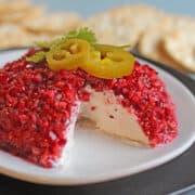 Cranberry jalapeno cream cheese dip on plate with jalapeno and cilantro garnish.