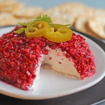 Cranberry jalapeno cream cheese dip on plate with jalapeno and cilantro garnish.