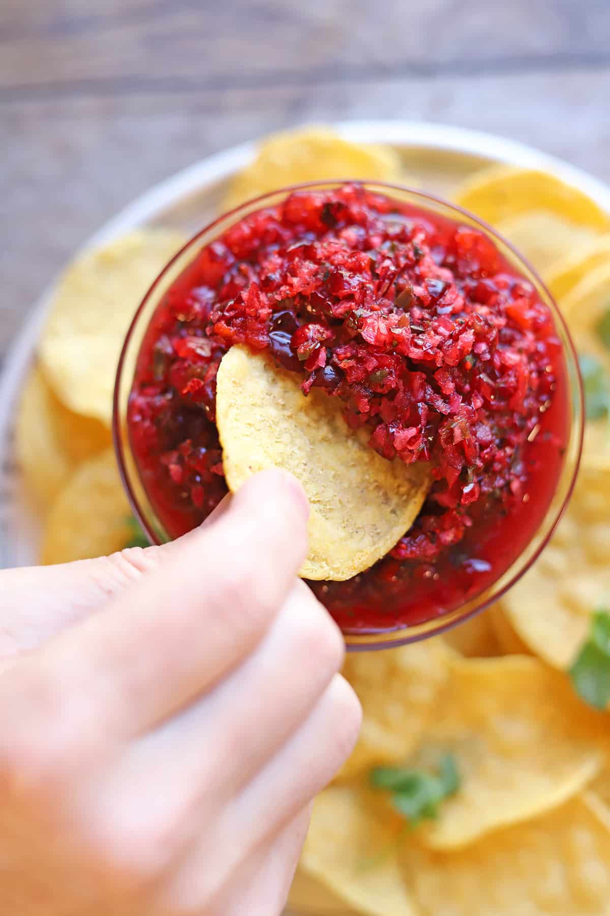 Tortilla chip being dunked into bright red cranberry salsa in bowl.