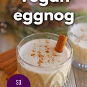 Text overlay: Vegan eggnog, so creamy, get the recipe at cadryskitchen.com. Glass of egg-free eggnog on table with sprinkle of cinnamon and cinnamon stick.
