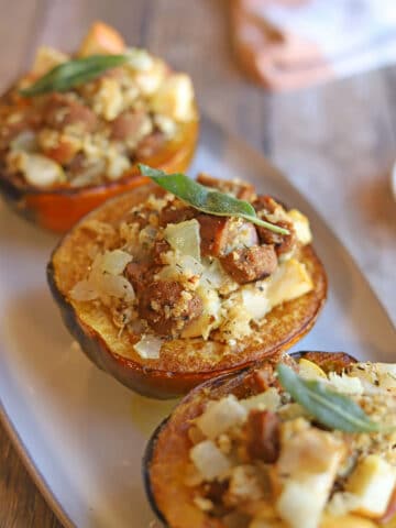 Three roasted acorn squash halves on platter, stuffed with vegan sausage and apple stuffing.