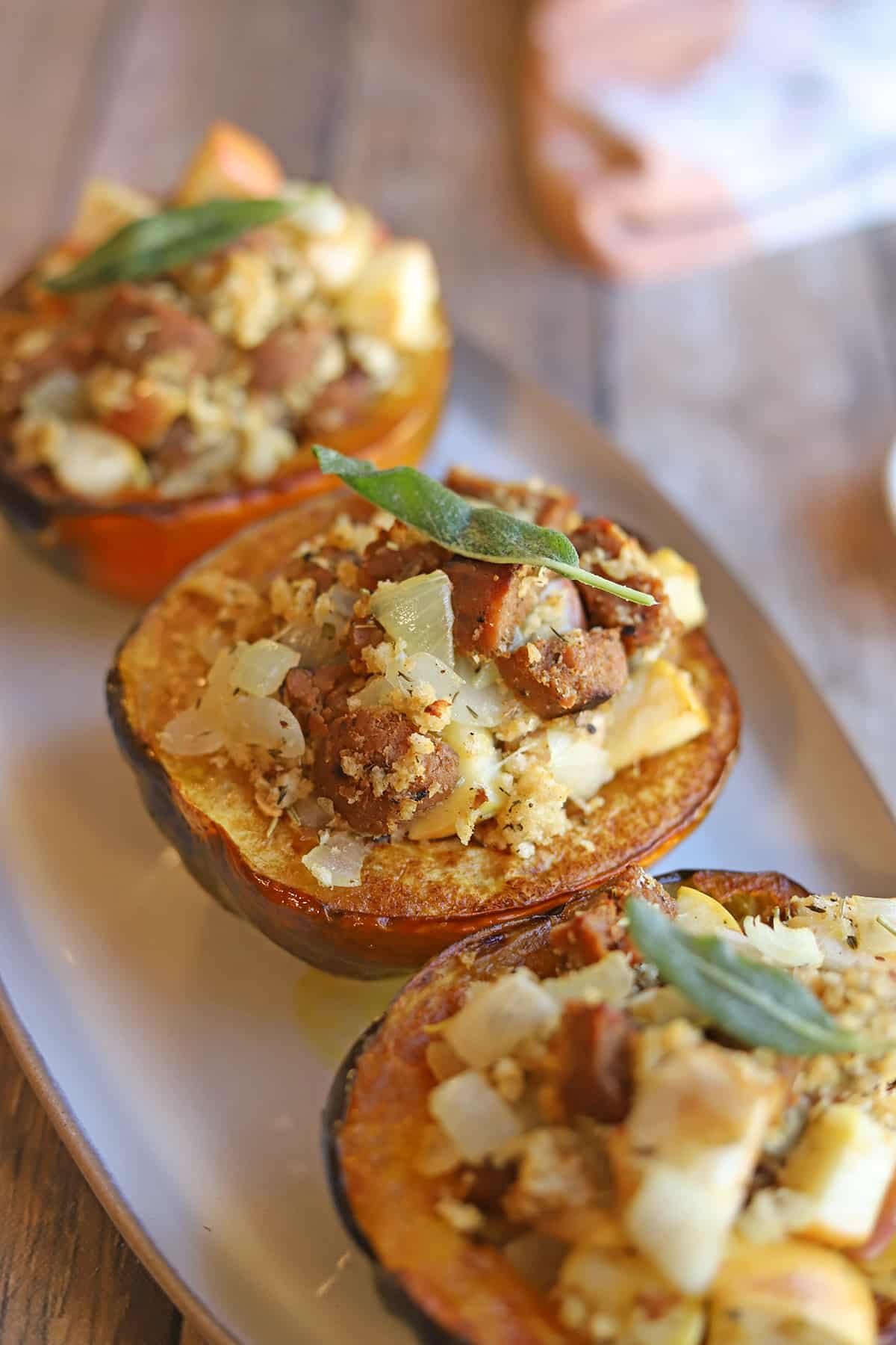 Three roasted acorn squash halves on platter, stuffed with vegan sausage and apple stuffing.