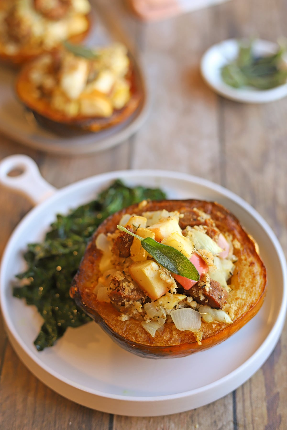 Apple and sausage stuffed acorn squash on plate with sauteed kale.