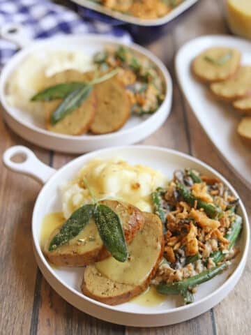 Slices of vegan turkey roast on plate with mashed potatoes and green bean casserole.