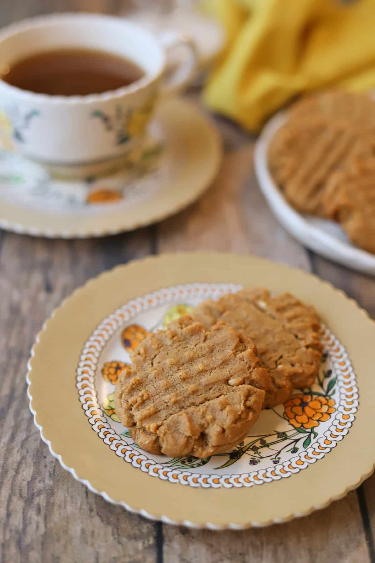 Two egg-free peanut butter cookies on plate by cup of tea.