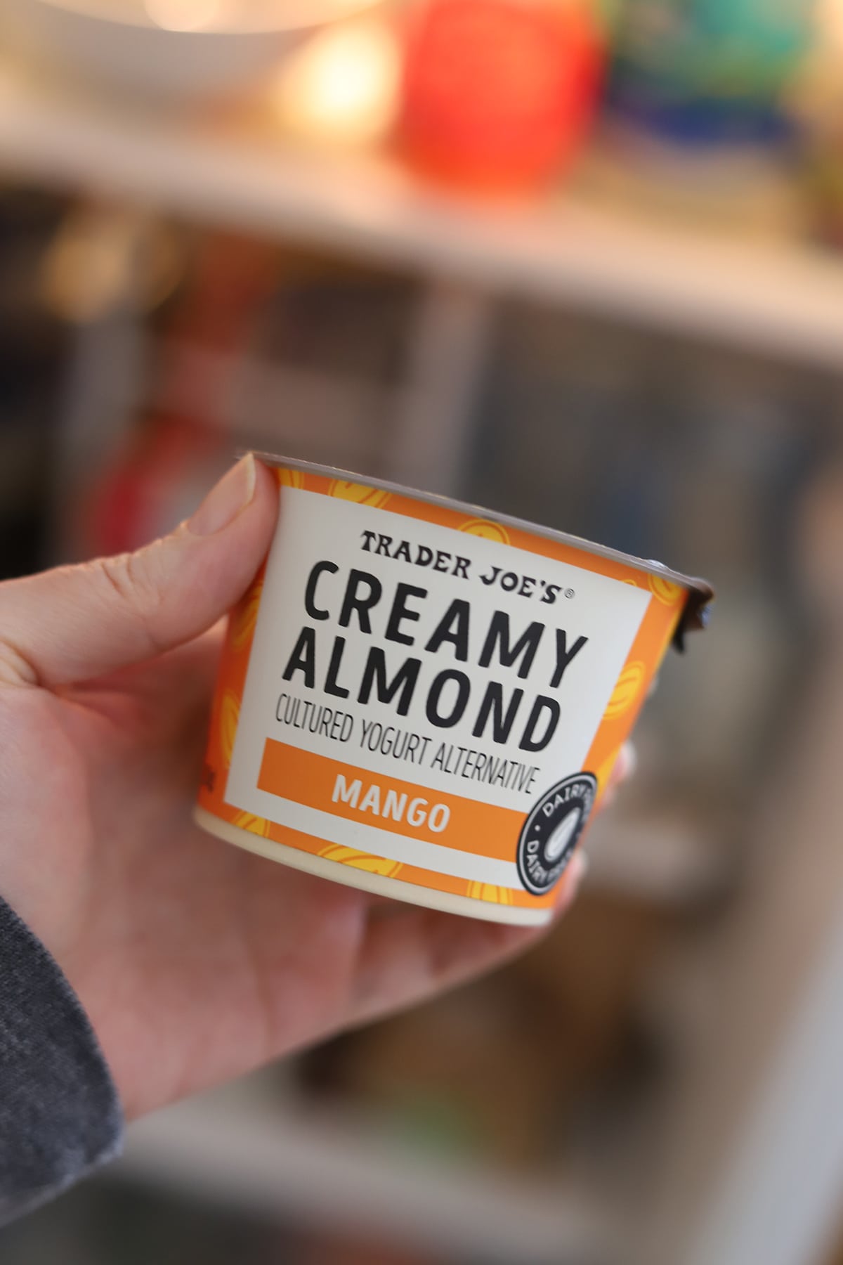 Hand holding container of mango flavored, creamy almond cultured yogurt alternative.