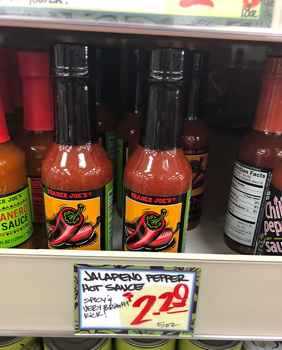 Bottles of jalapeno pepper hot sauce on shelf at Trader Joe's.
