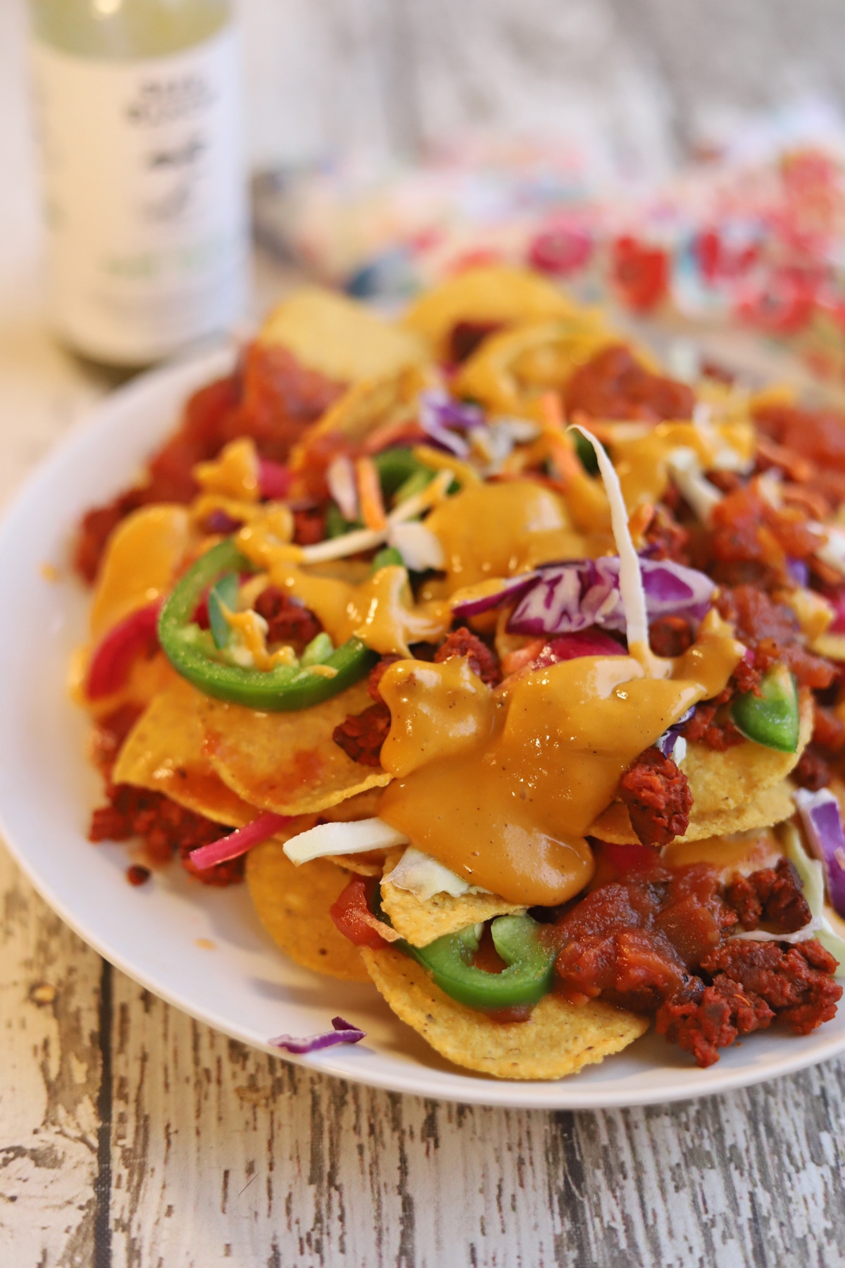 Vegan queso poured over nachos with soyrizo, jalapenos, and shredded cabbage mix on plate.