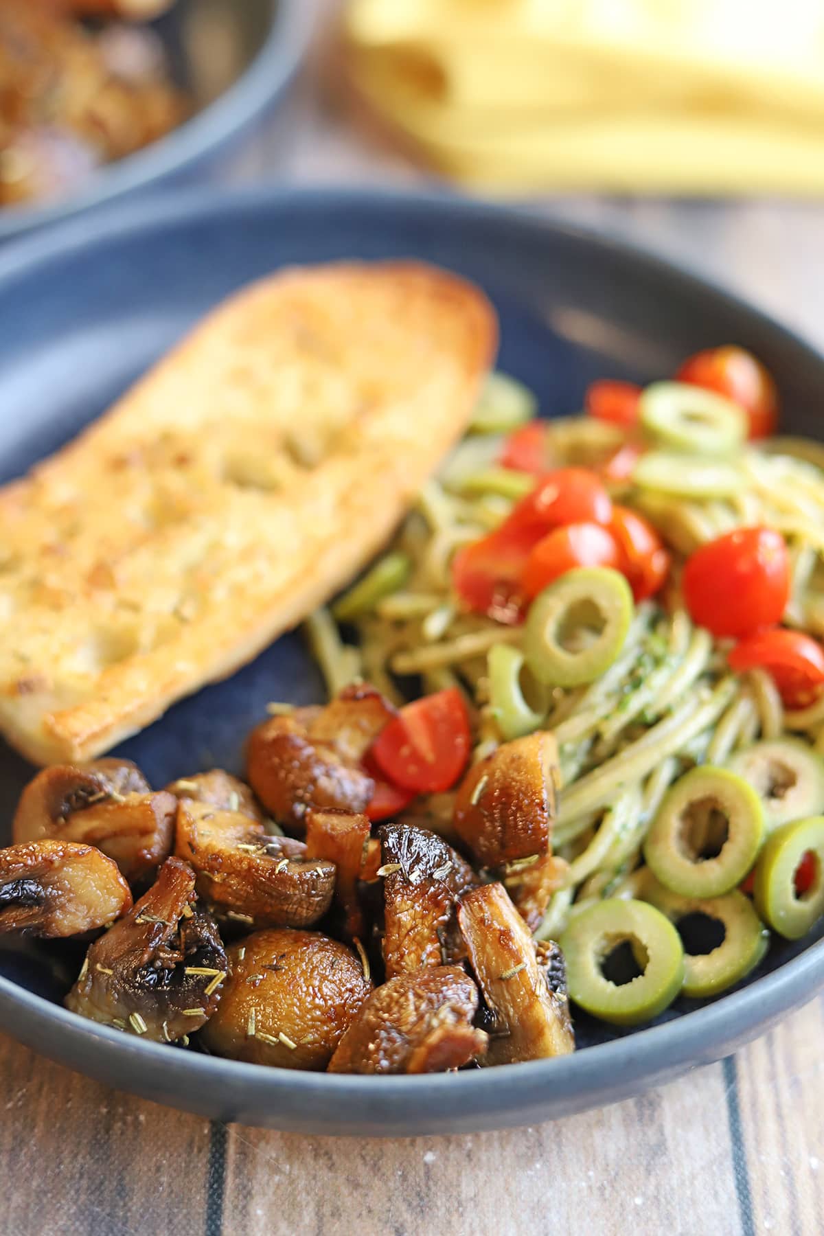 Crispy air fryer mushrooms with garlic, rosemary, and thyme, on plate with garlic bread and pasta with pesto and olives.