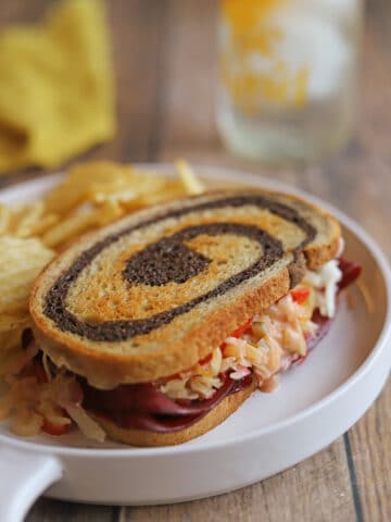 Thinly sliced corned beef style seitan on vegan reuben with sauerkraut and Thousand Island by pile of potato chips.