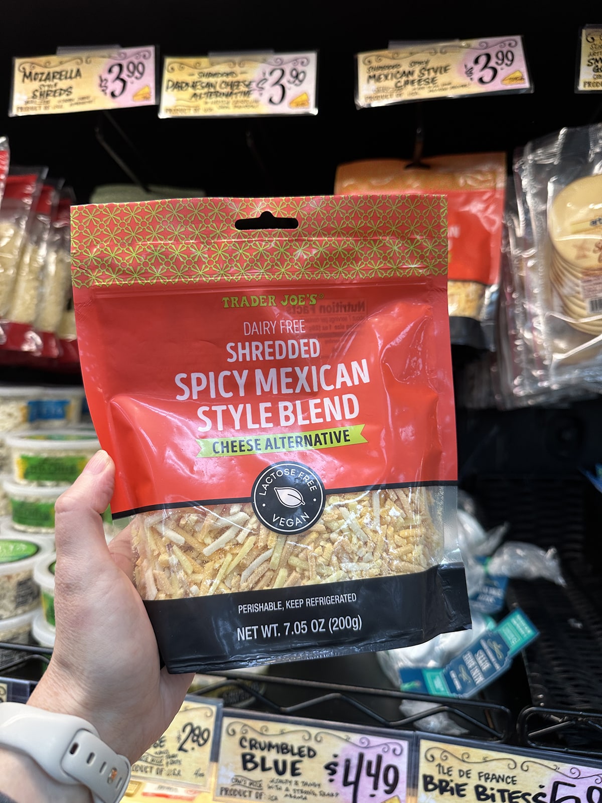 Hand holding Trader Joe's dairy free shredded spicy Mexican style blend cheese alternative.