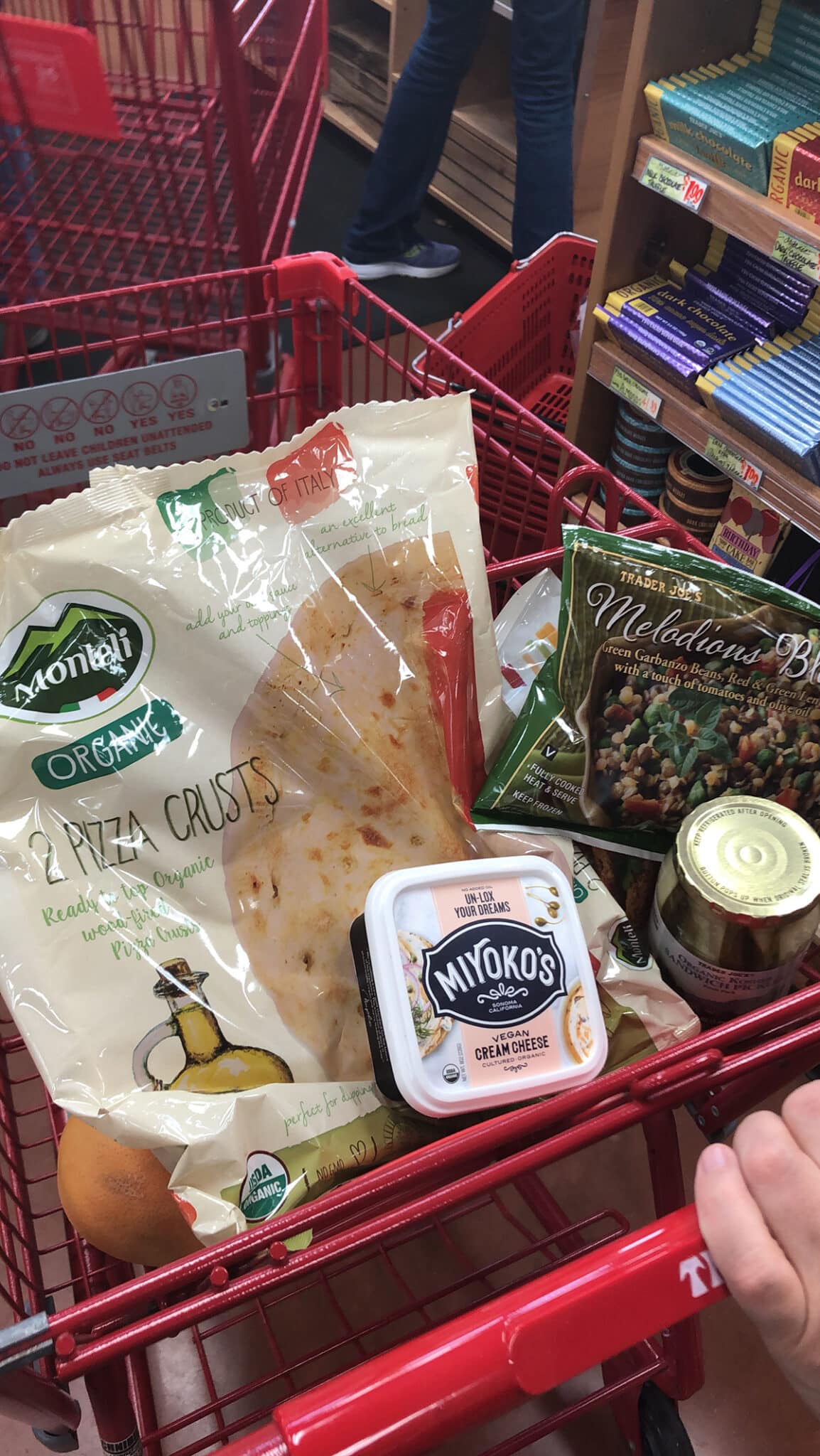 Trader Joe's shopping cart with Monteli pizza crusts, Miyoko's cream cheese, grapefruit, and pickles.
