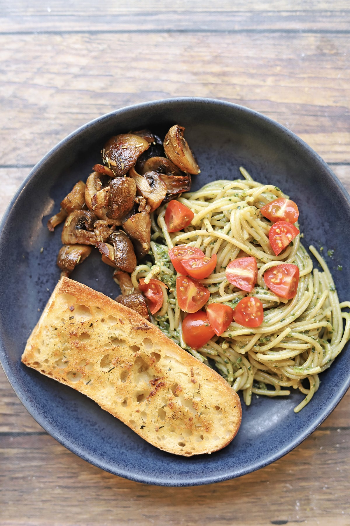 Garlicky, herb-roasted air fryer mushrooms on plate with pesto pasta and garlic bread.