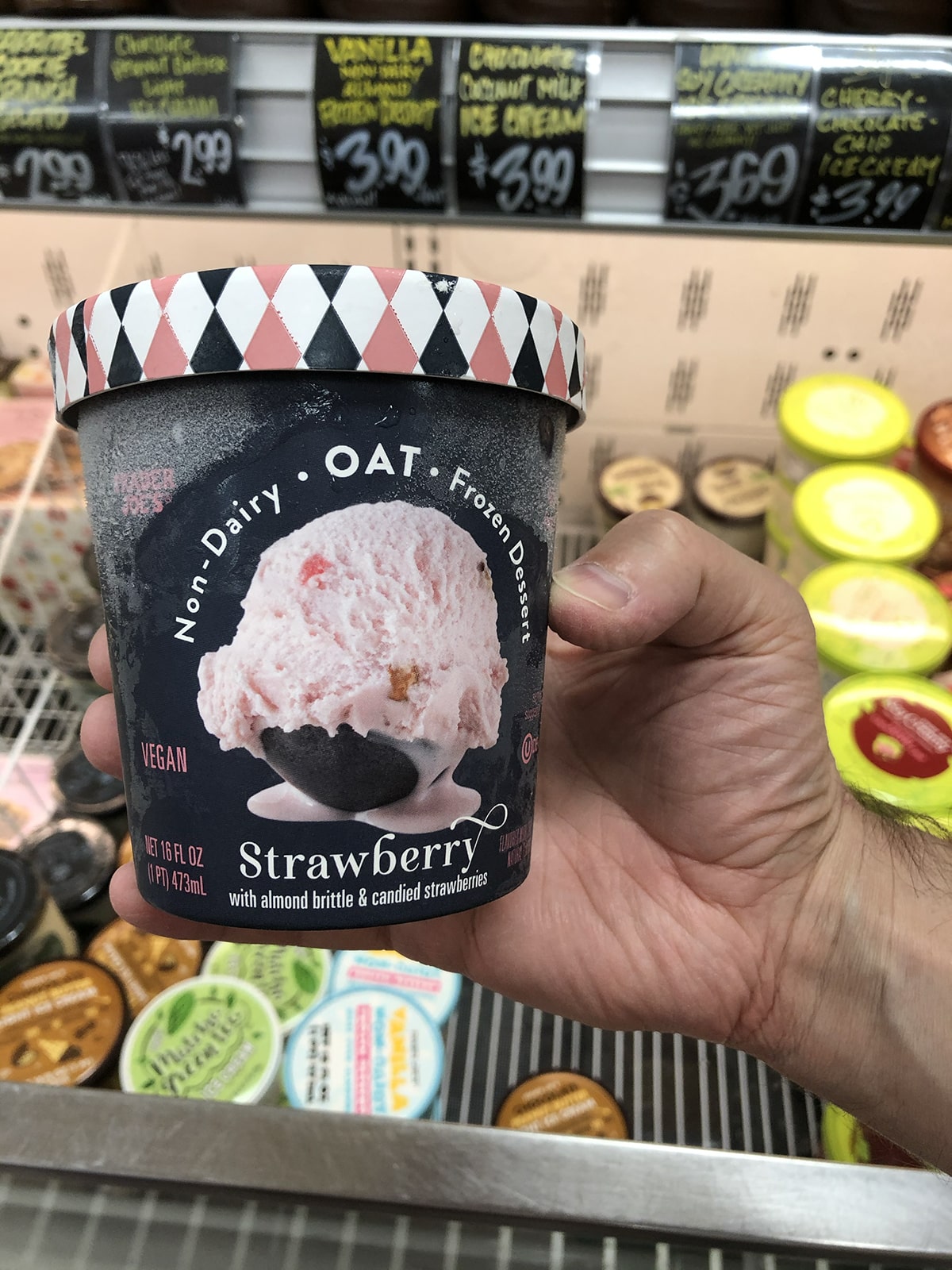 Hand holding pint of non-dairy oat frozen dessert, strawberry with almond brittle and candied strawberries.