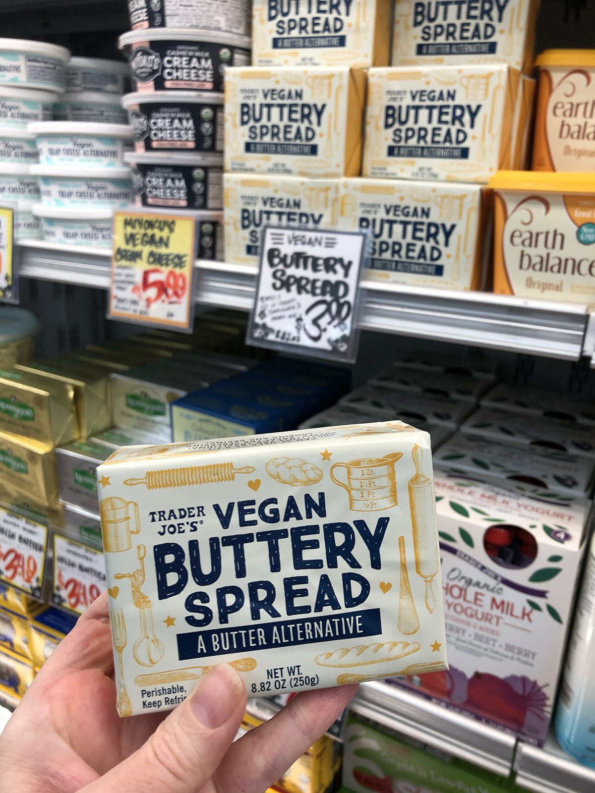 Hand holding vegan buttery spread butter alternative in cold case at Trader Joe's.