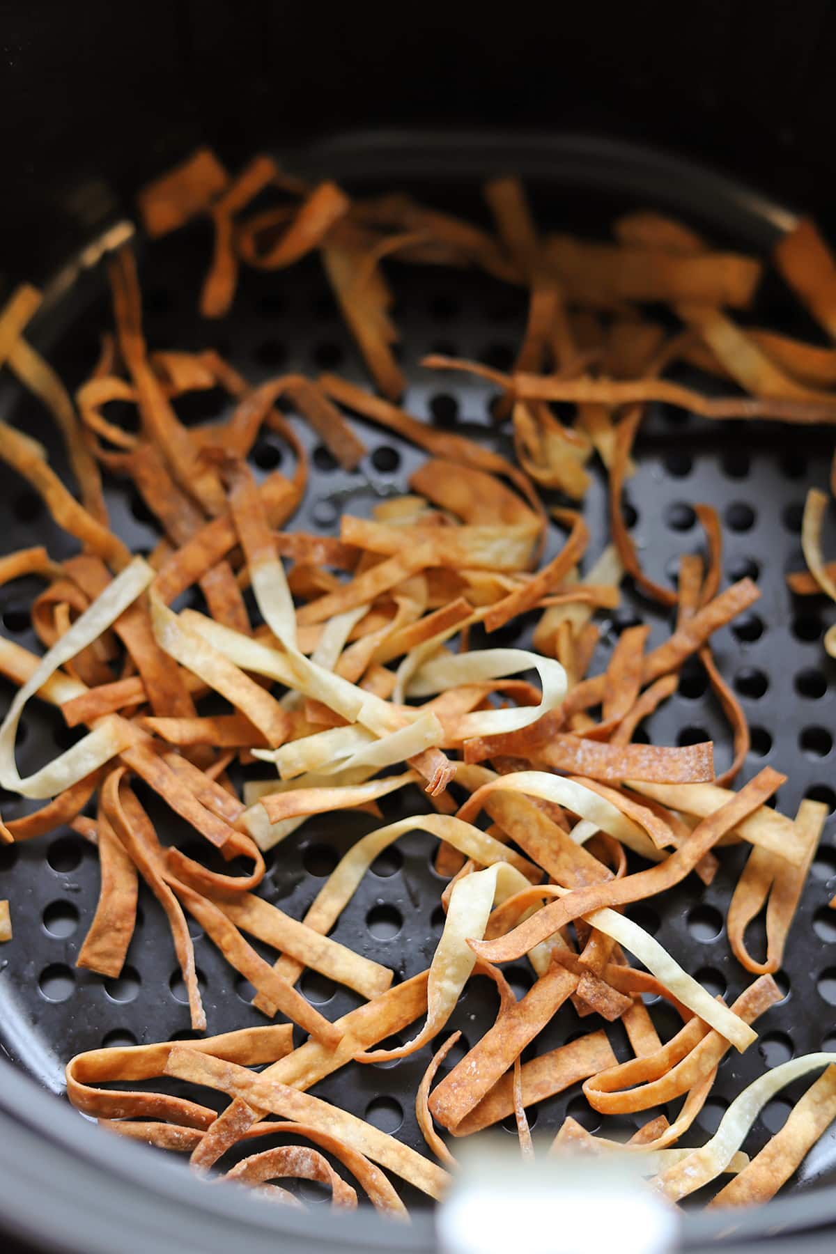 Crispy wonton strips in air fryer basket.