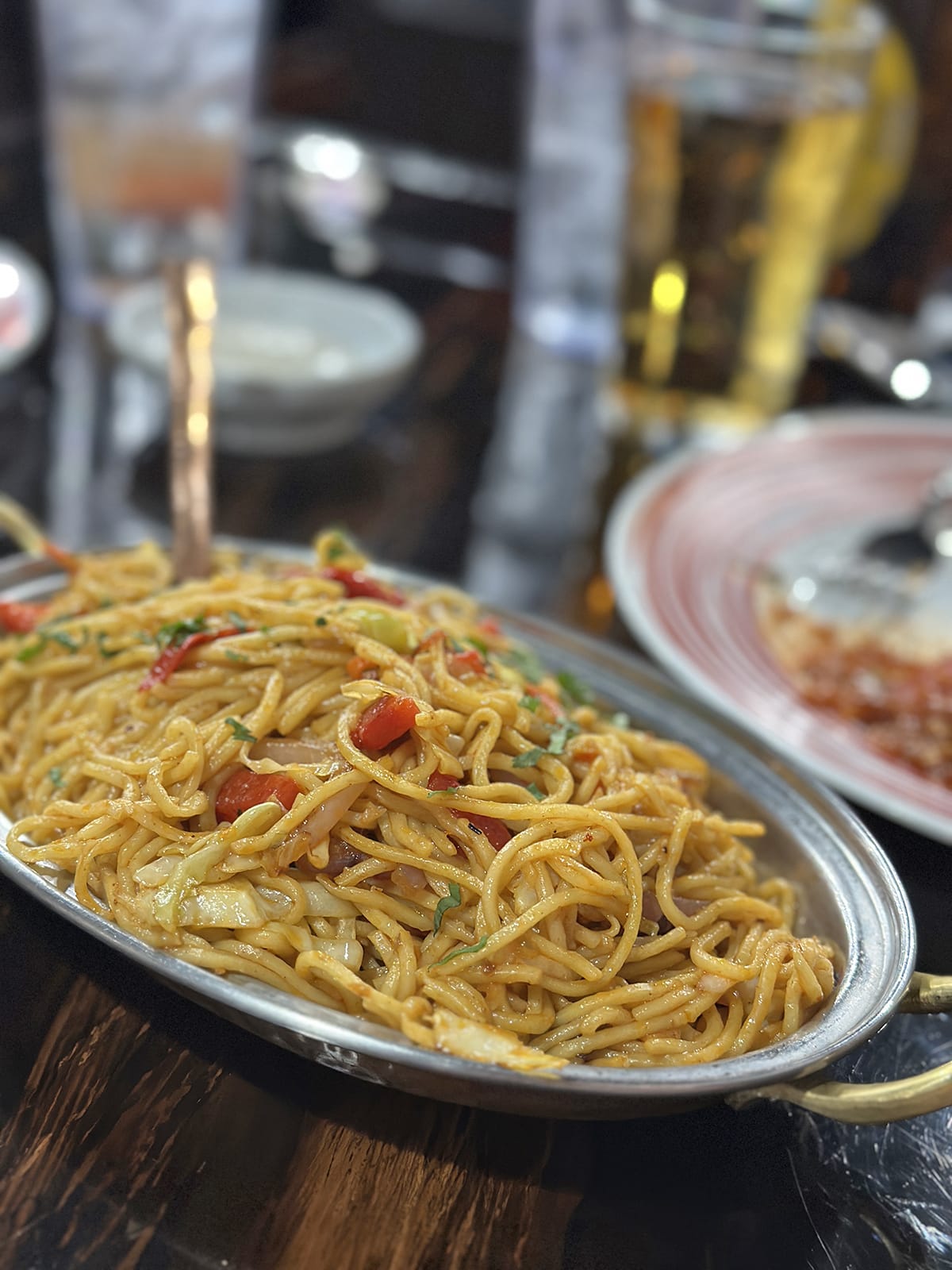 Hakka noodles in metal bowl with peppers.