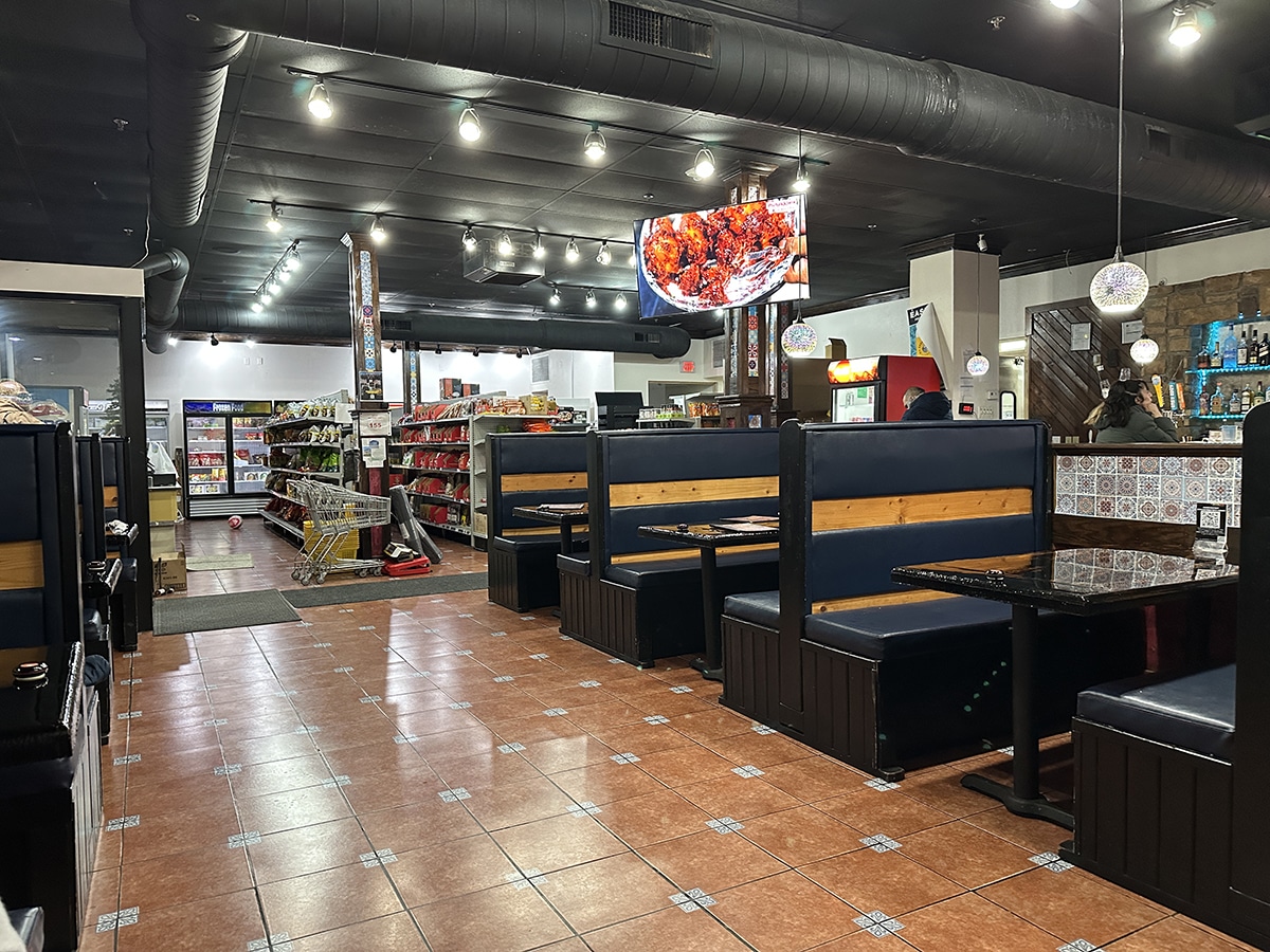 Interior Paradise Indian grill with booths and small grocery store, plus cooking show playing on television set.
