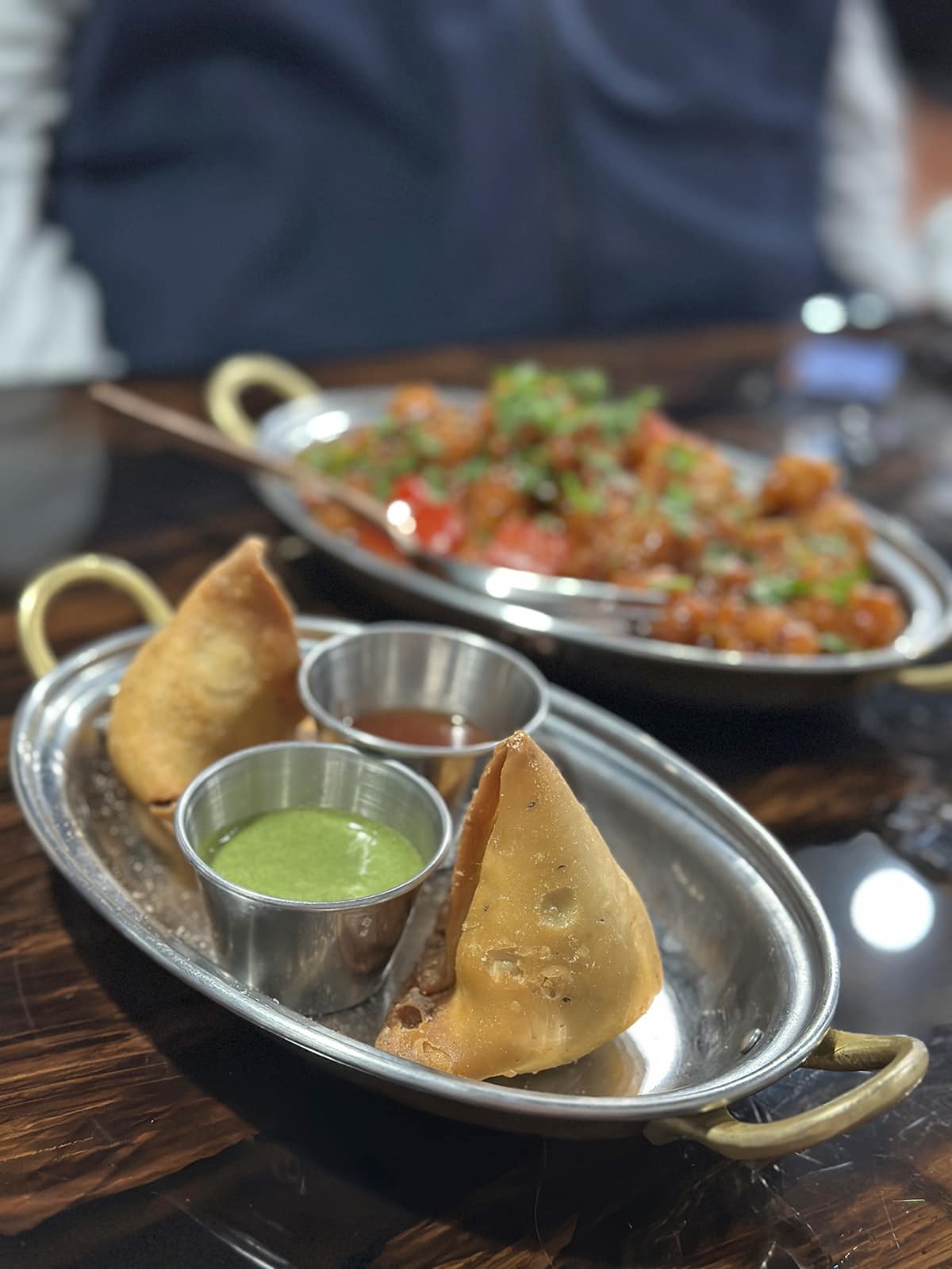 Vegetable samosas on tray with cilantro chutney and tamarind chutney.