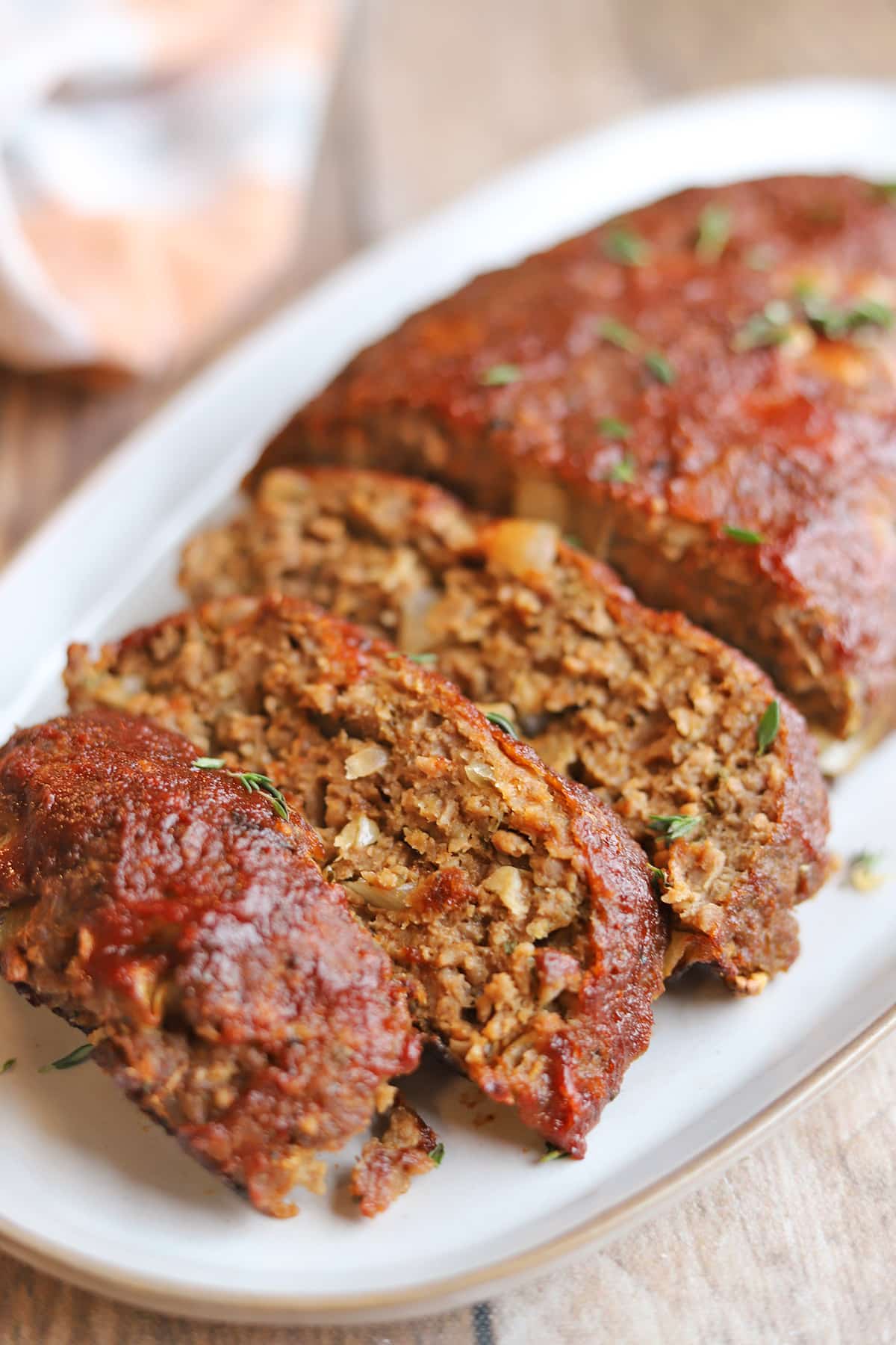 Thick slices of juicy vegan meatloaf with ketchup glaze on platter.