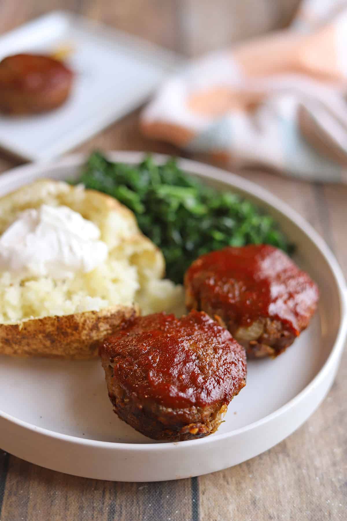 Mini vegan meatloafs on plate with baked potato and kale.