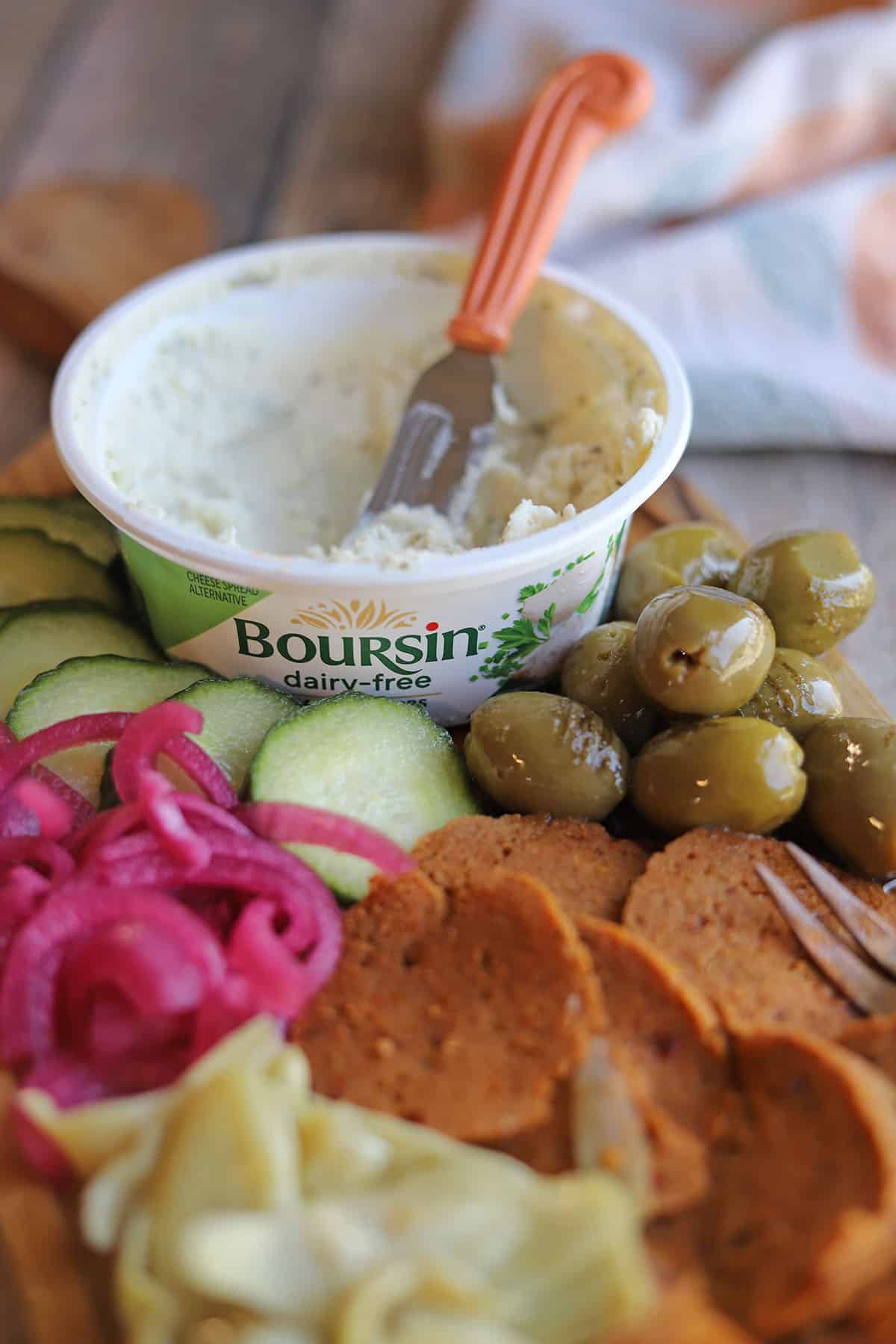 Container of Boursin dairy-free garlic and herbs spread with olives, cucumbers, pickled onions, and vegan pepperoni.