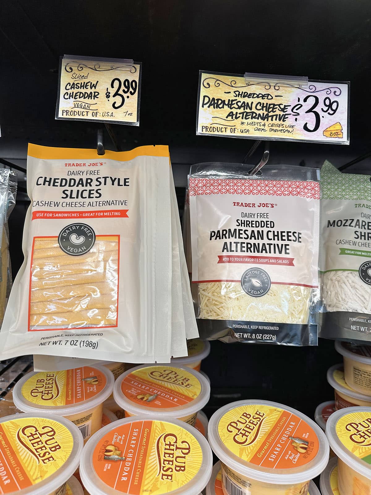 Dairy free cheddar style slices and shredded parmesan cheese alternative on display at Trader Joe's.