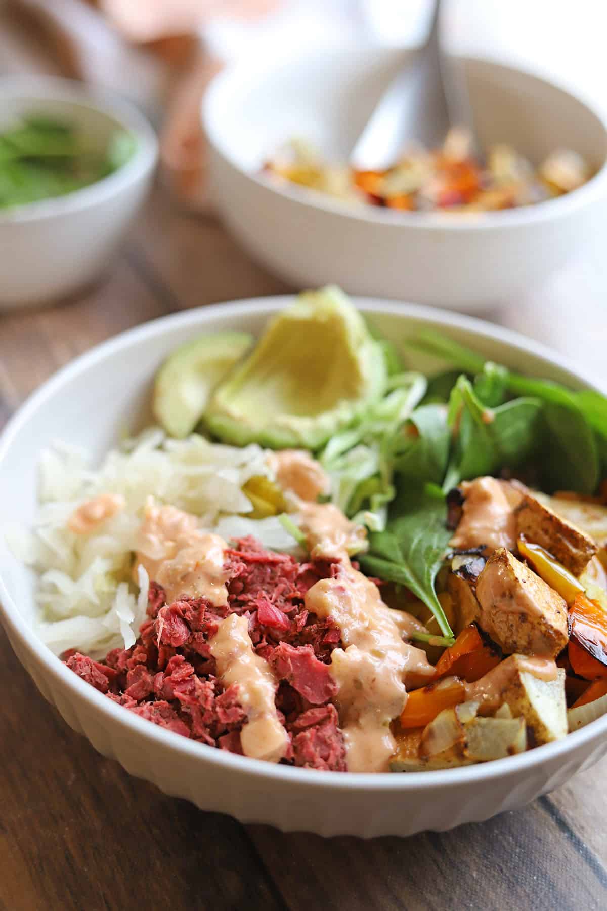 Gluten-free reuben bowl with corned jackfruit, roasted potatoes, sauerkraut, and baby spinach topped with non-dairy dressing.
