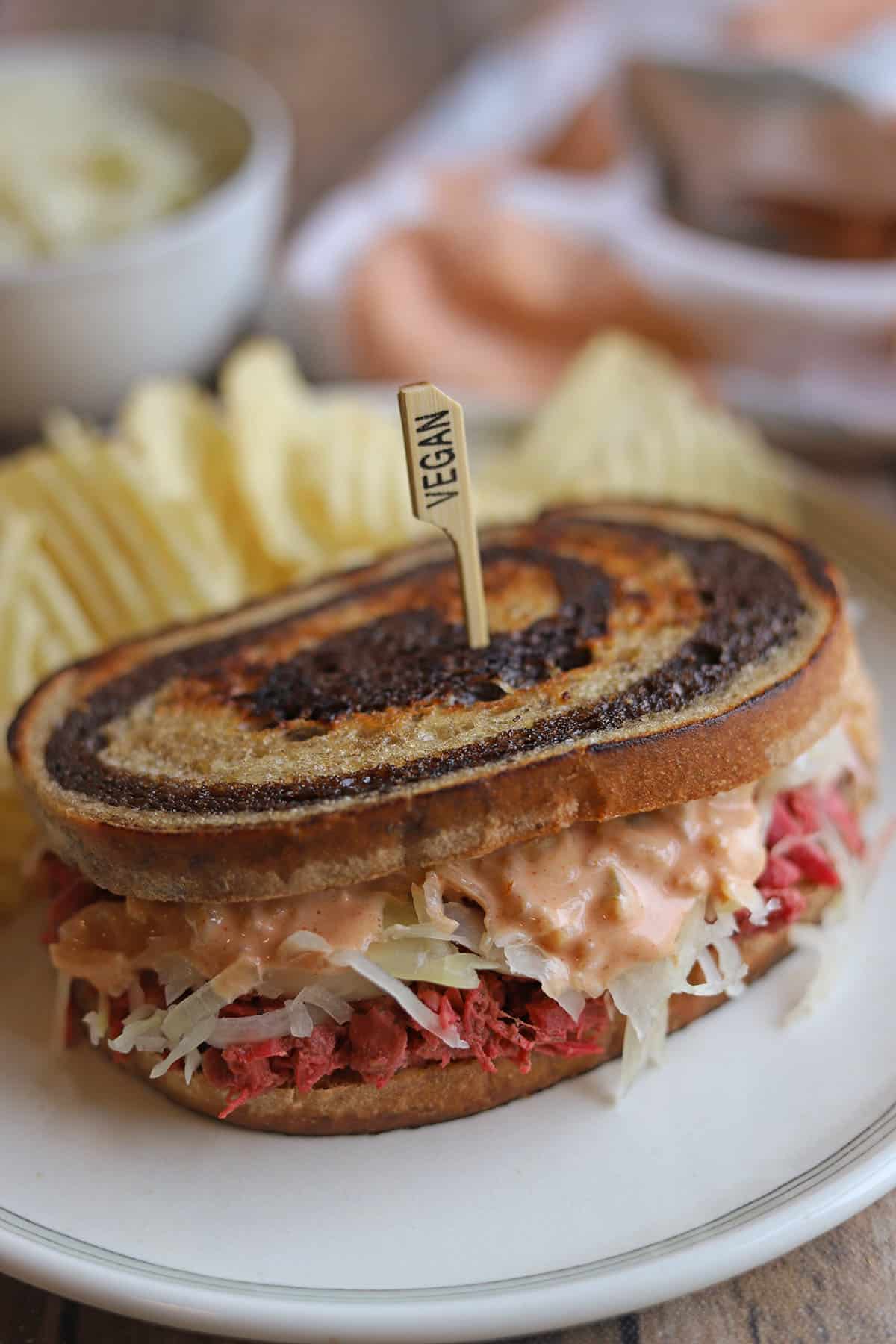 Creamy vegan Thousand Island dressing dripping down sauerkraut and corned jackfruit on vegan reuben sandwich.