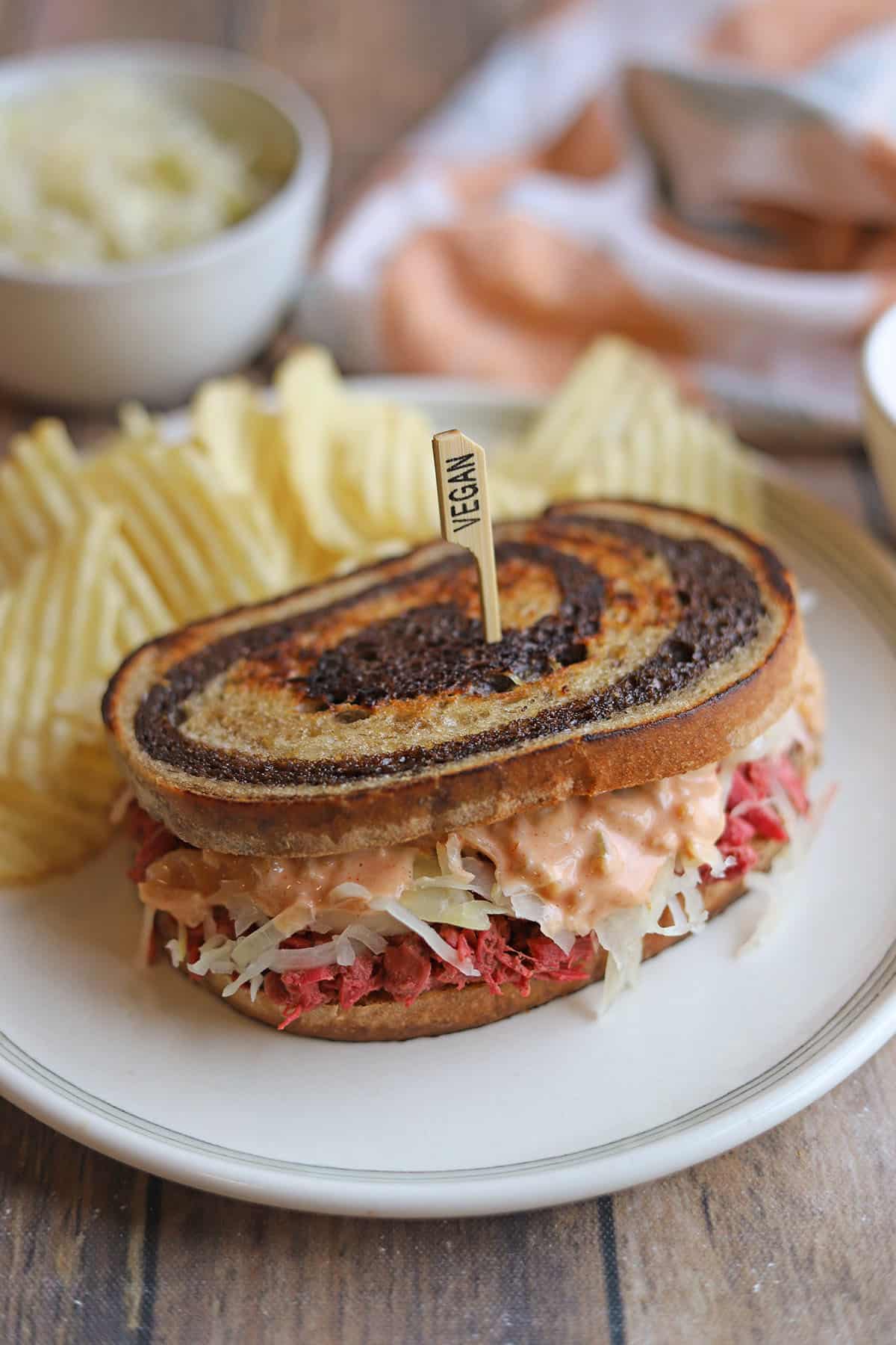 Vegan corned beef-style jackfruit reuben on plate with potato chips.