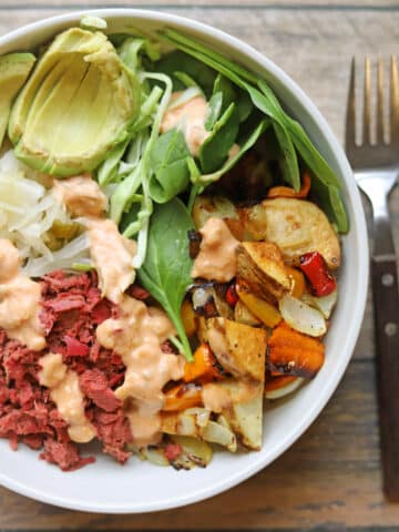 Vegan reuben bowl with jackfruit corned beef, baby spinach, roasted potato hash, and sauerkraut drizzled with vegan Thousand Island dressing.