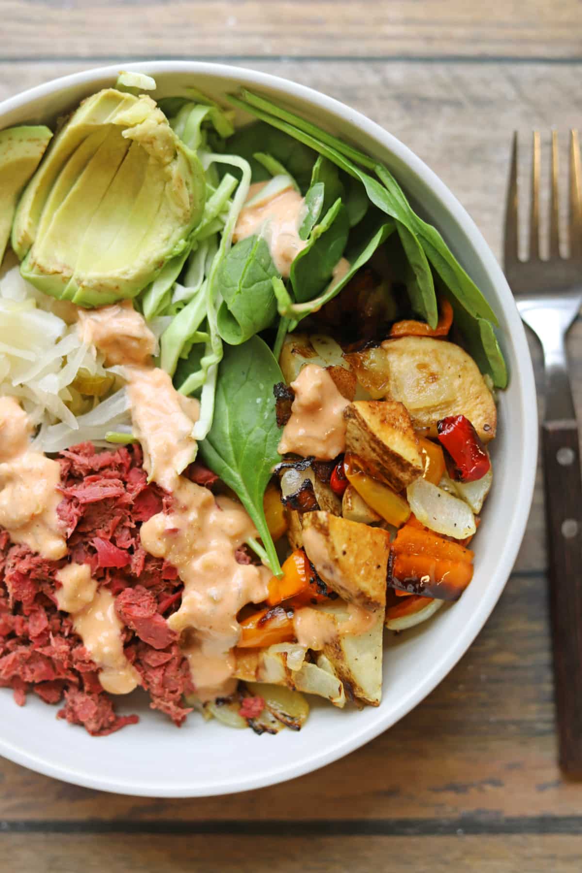 Vegan reuben bowl with jackfruit corned beef, baby spinach, roasted potato hash, and sauerkraut drizzled with vegan Thousand Island dressing.