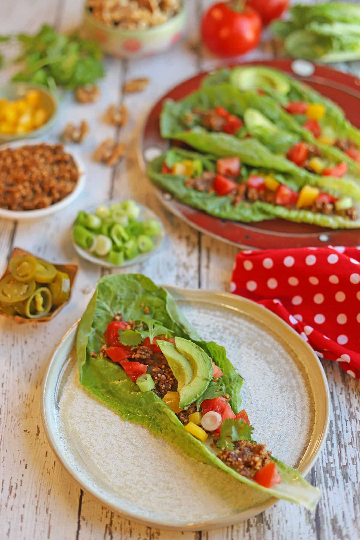 Raw walnut tacos topped with avocado, bell pepper, and tomatoes laid out on table.