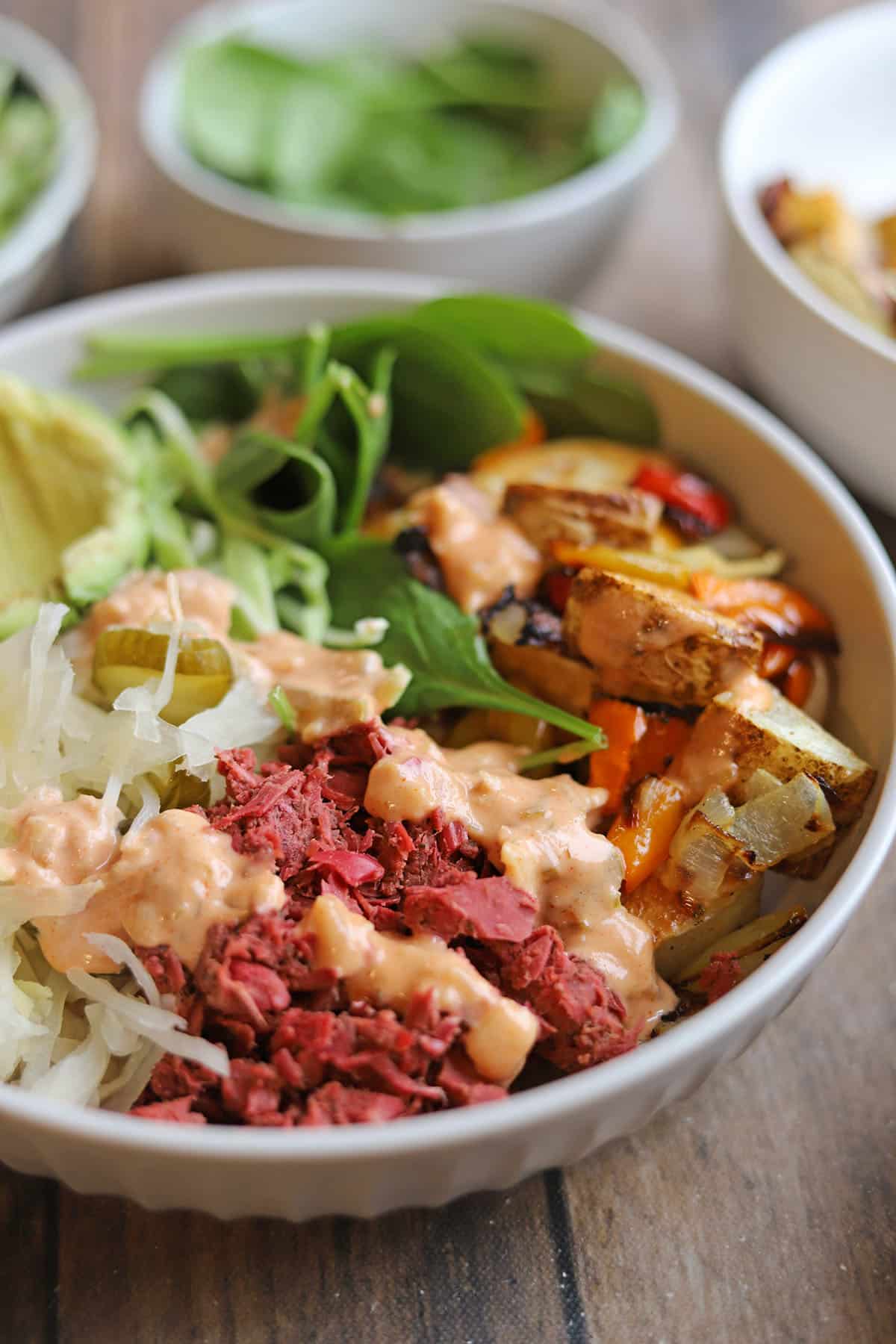 Bright pink jackfruit corned beef in vegan reuben bowl with sauerkraut, spinach, and roasted potatoes.