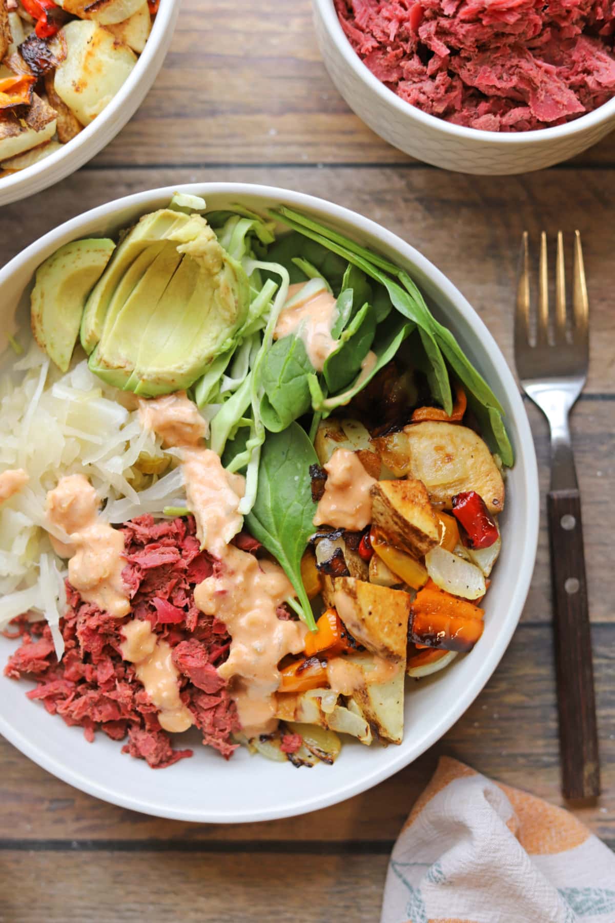 Vegan reuben bowl with corned beef-style jackfruit, avocado, sauerkraut, spinach, and cabbage on a bed of roasted potatoes.