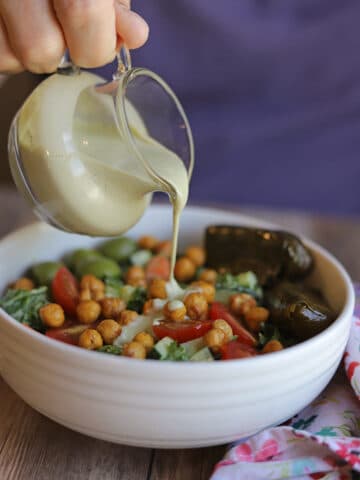 Creamy cashew-based dressing being poured onto kale salad with roasted chickpeas and dolmas.